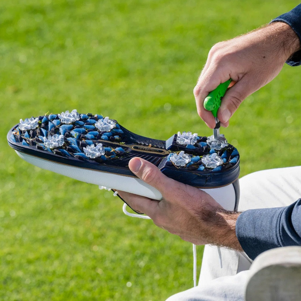 Golfer using a green spike wrench on a golf shoe sole outdoors