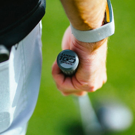 Close-up of a golf grip end cap marked Lamkin 100 Standard, held by a golfer